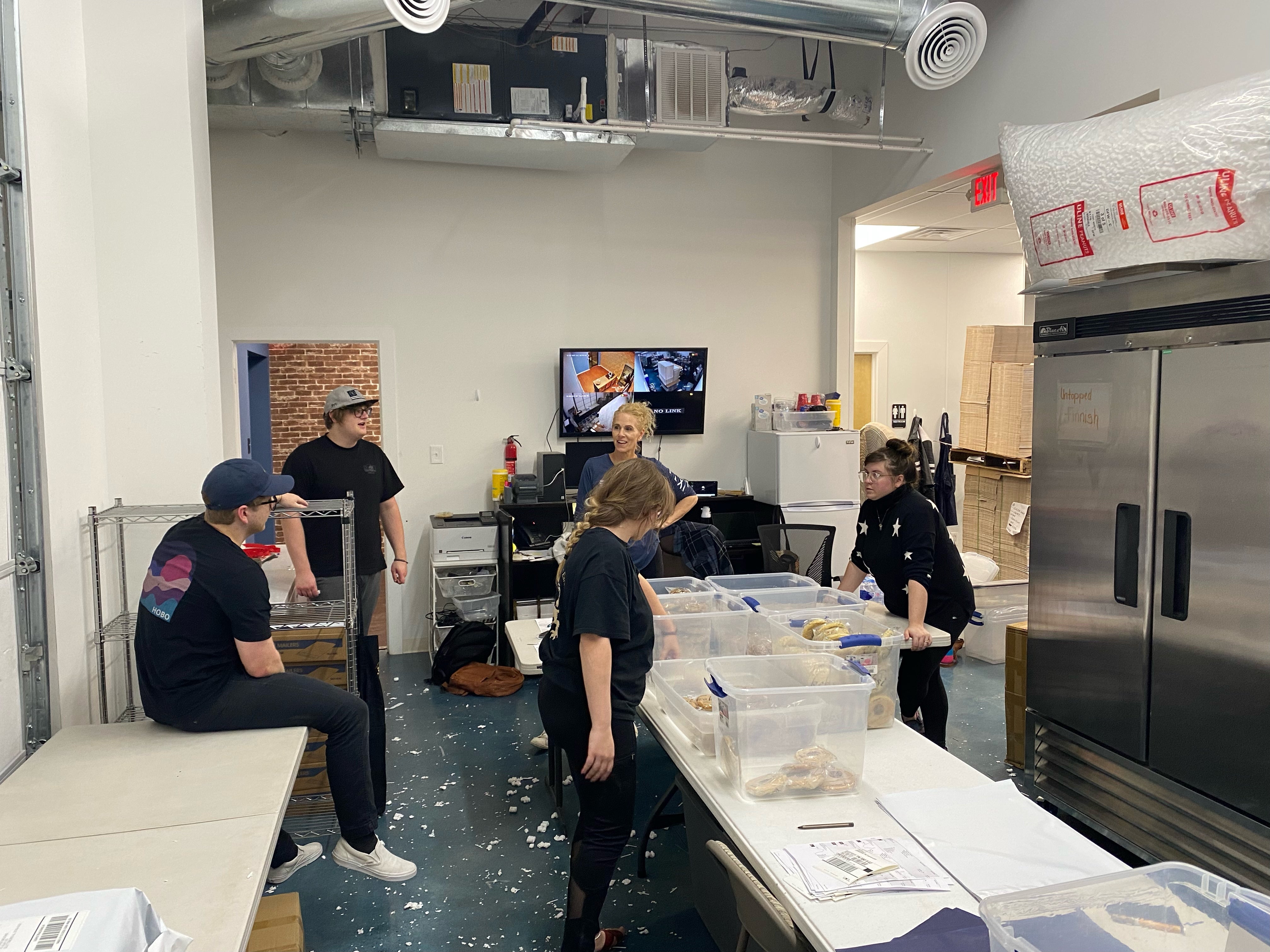 People in a kitchen or food preparation area with equipment and supplies.