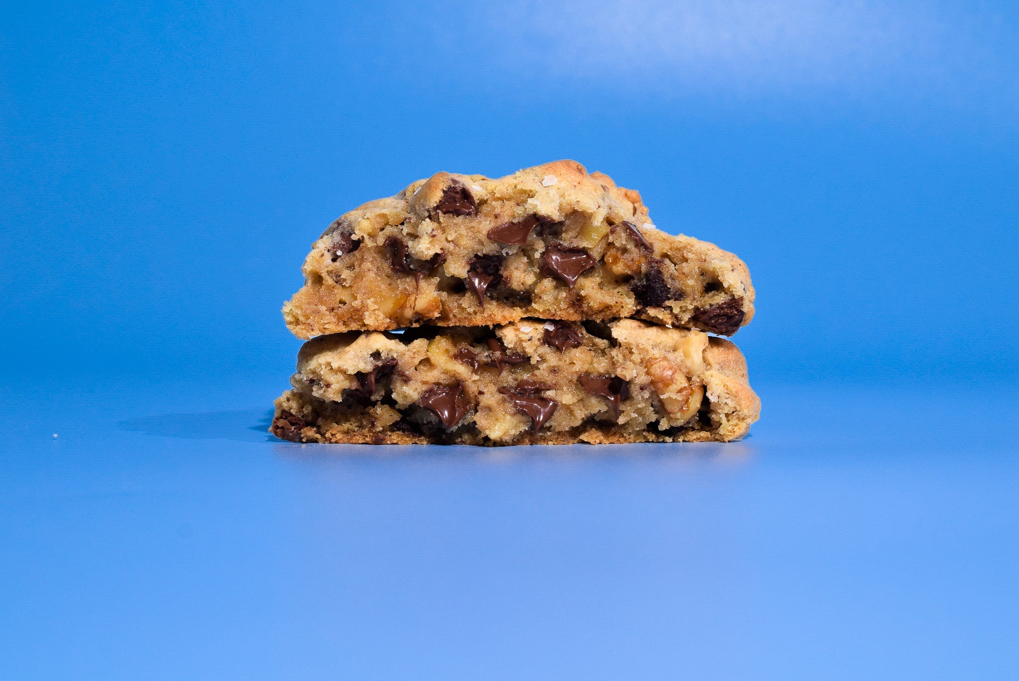 Two stacked New York Chocolate Chip cookies on a blue background.