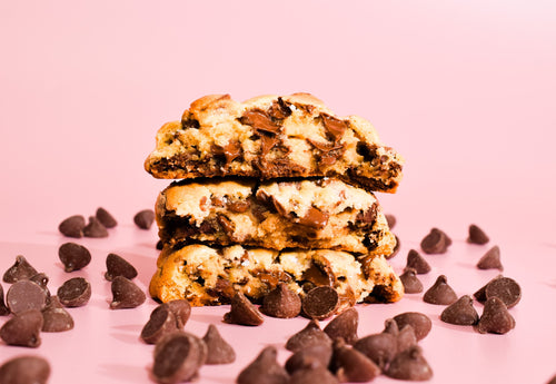 Texas Chocolate Chip Cookies Stacked on top of each other on a pink background with scattered chocolate chips.