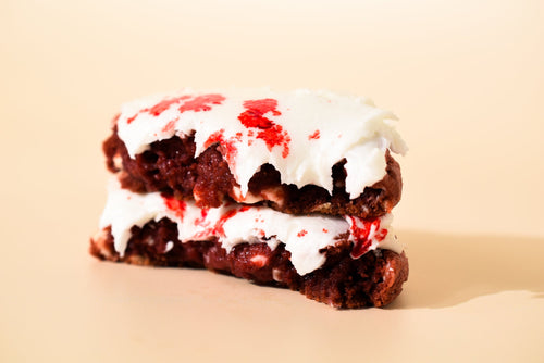 Blood Velvet cookie halves stacked, showing red velvet crumb under thick white icing
