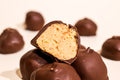 Chocolate-covered confection pieces on a white background, with one piece broken in half to show a creamy peanut butter-like filling.