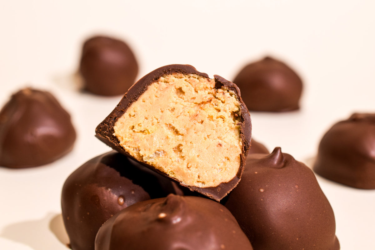 Chocolate-covered confection pieces on a white background, with one piece broken in half to show a creamy peanut butter-like filling.