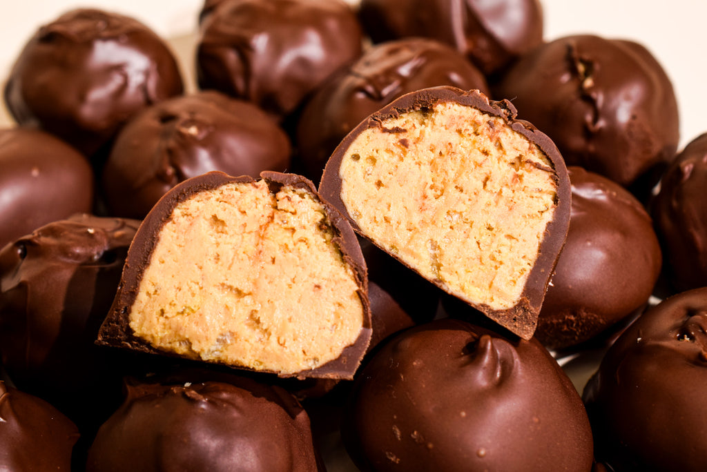 Chocolate-covered truffles with one cut open to show a creamy, light tan cookie-like filling, photographed close up against a warm beige background.