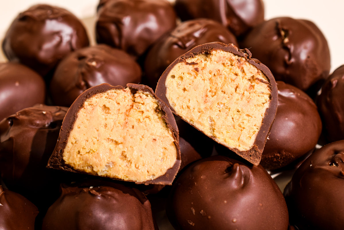 Chocolate-covered truffles with one cut open to show a creamy, light tan cookie-like filling, photographed close up against a warm beige background.