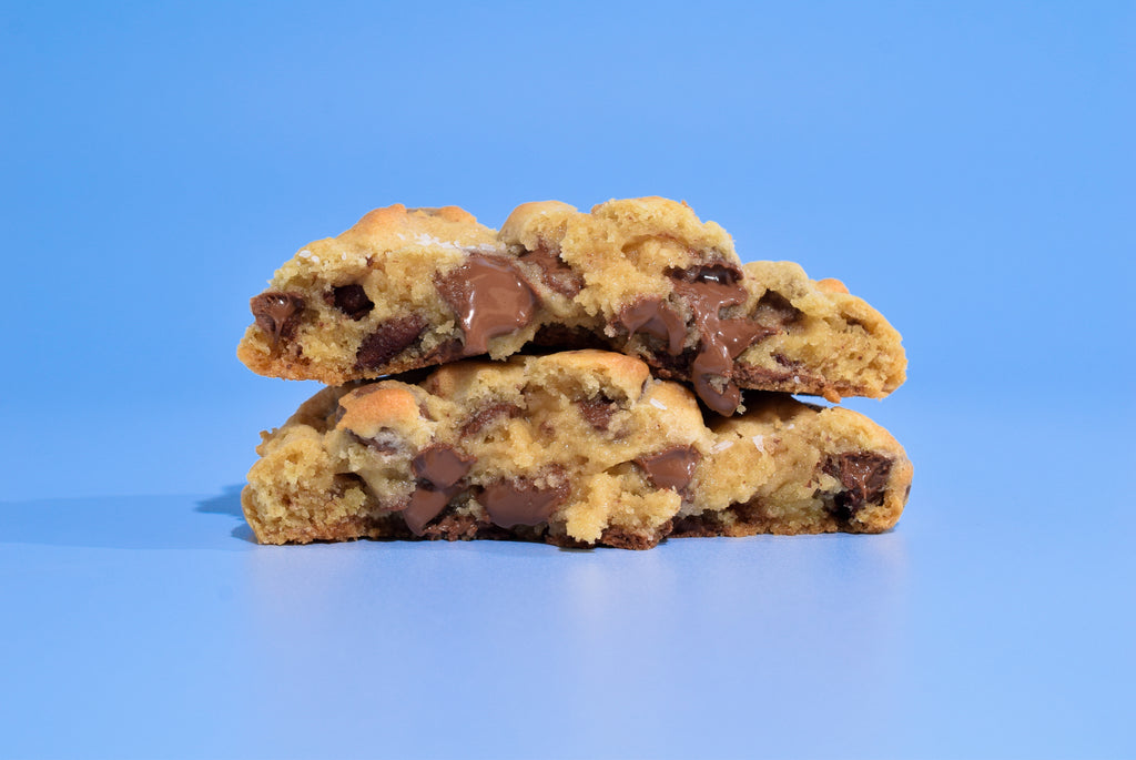 Two stacked chocolate chip cookies on a solid blue background.