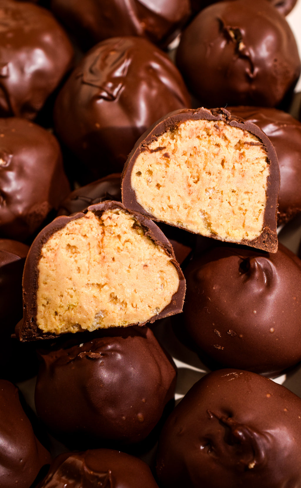 Chocolate-covered cookie dough truffles, with one cut open to show a light tan cookie dough filling, surrounded by more whole truffles.