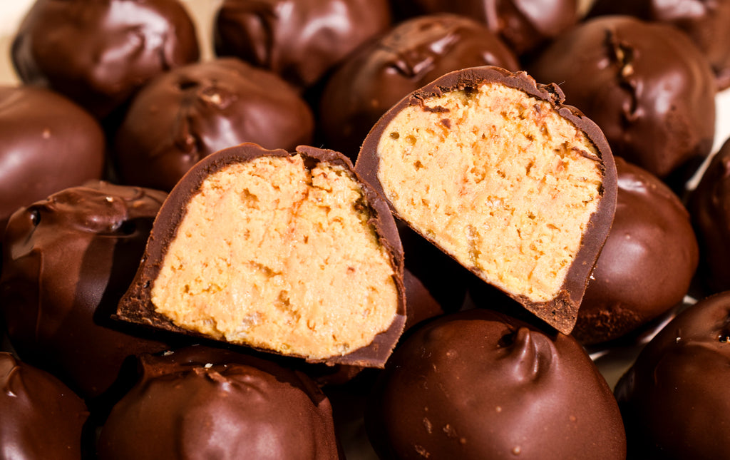 Close-up of chocolate-covered confectionery balls, with two halves broken open to show a creamy tan filling, set against a background of similar chocolates.