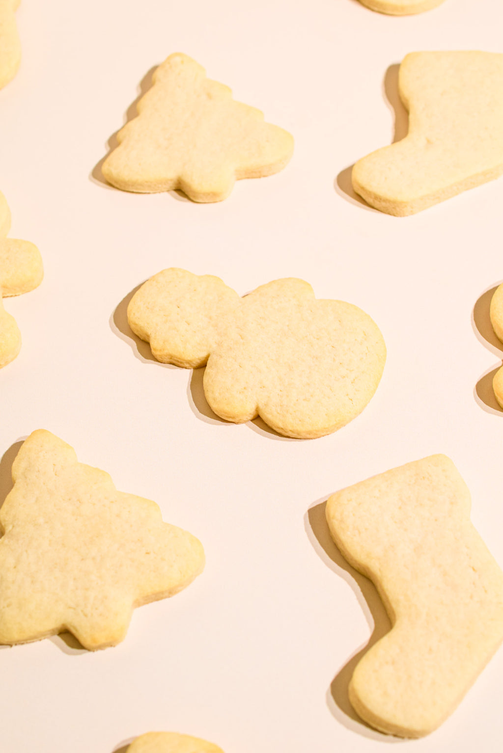 Decorated sugar cookies in Christmas shapes, including a Christmas tree, a stocking, and a Santa silhouette, arranged on a warm cream background.