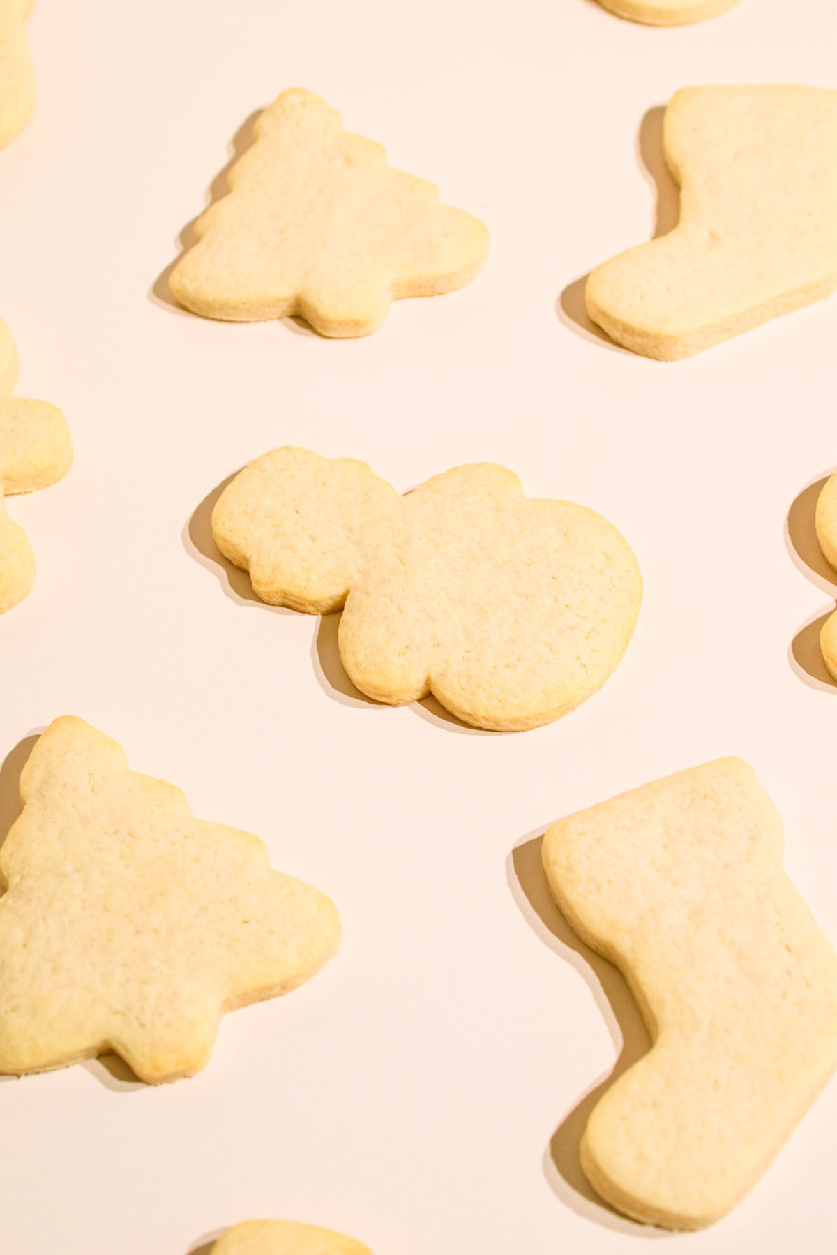 Decorated sugar cookies in Christmas shapes, including a Christmas tree, a stocking, and a Santa silhouette, arranged on a warm cream background.