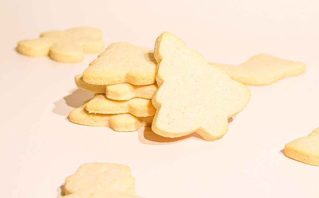 A pile of pale yellow, sugar-dusted Christmas tree-shaped cookies on a warm, off-white background.