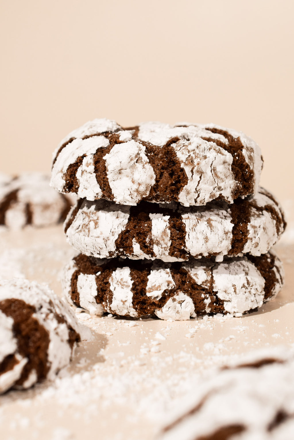 Three stacked chocolate crumb cookies dusted with powdered sugar on a warm beige background.