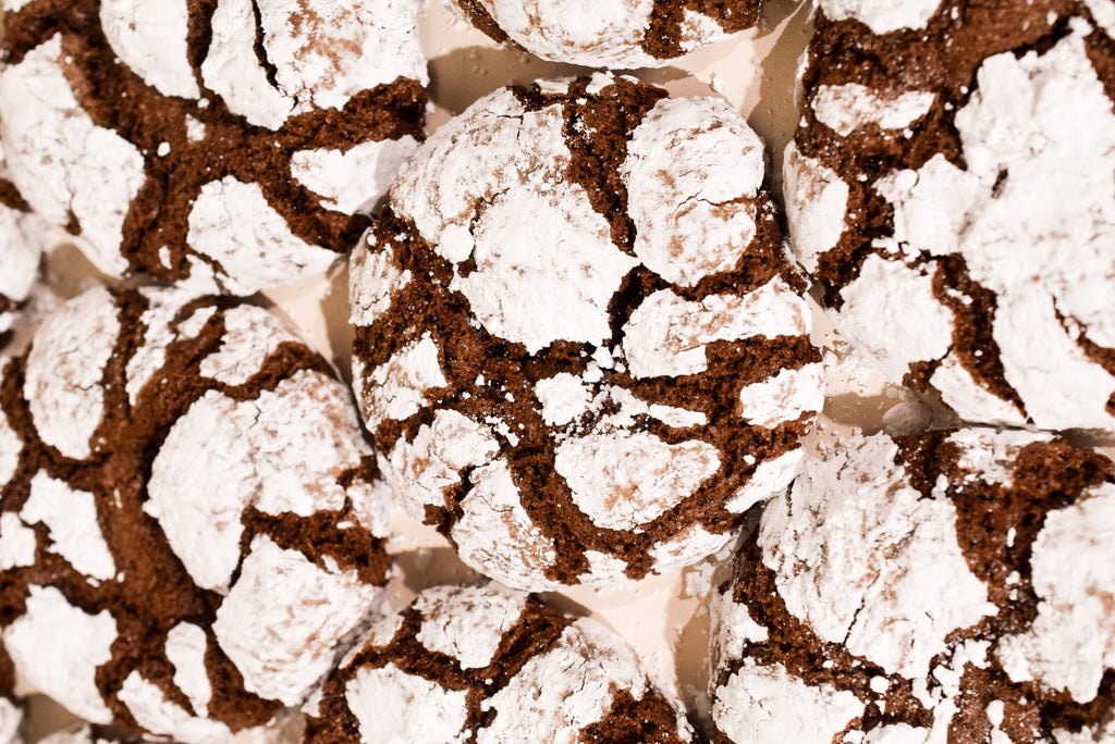 A close-up top-down view of several chocolate crinkle cookies dusted with powdered sugar, filling the frame.