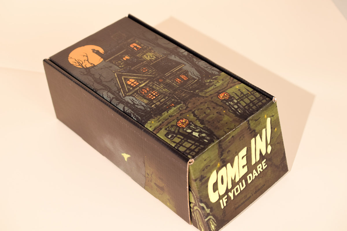A rectangular cardboard box with a spooky haunted-house illustration and the text 'COME IN! IF YOU DARE' on a plain light background.