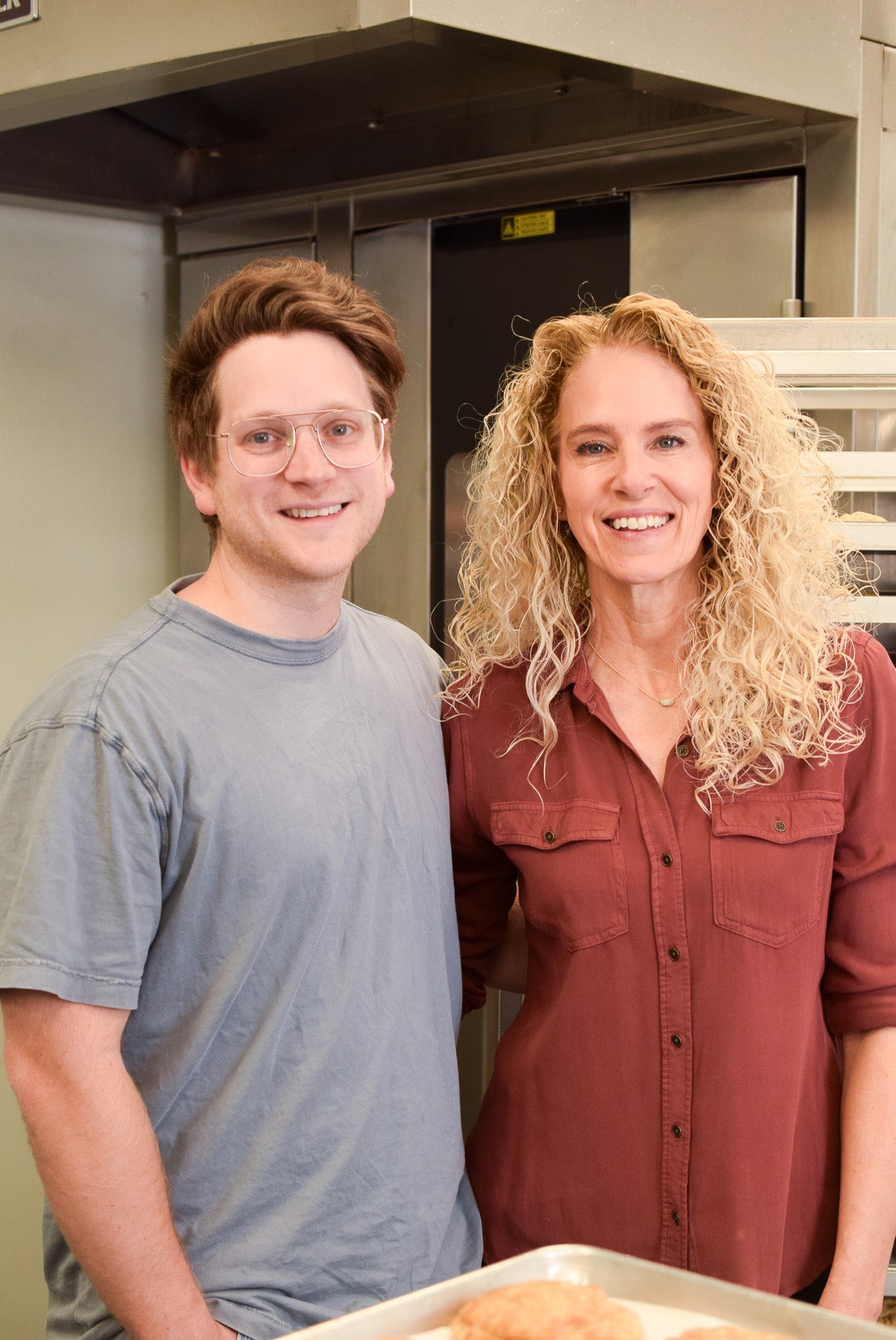 The two owners of Keksi Cookies standing together in the kitchen smiling.