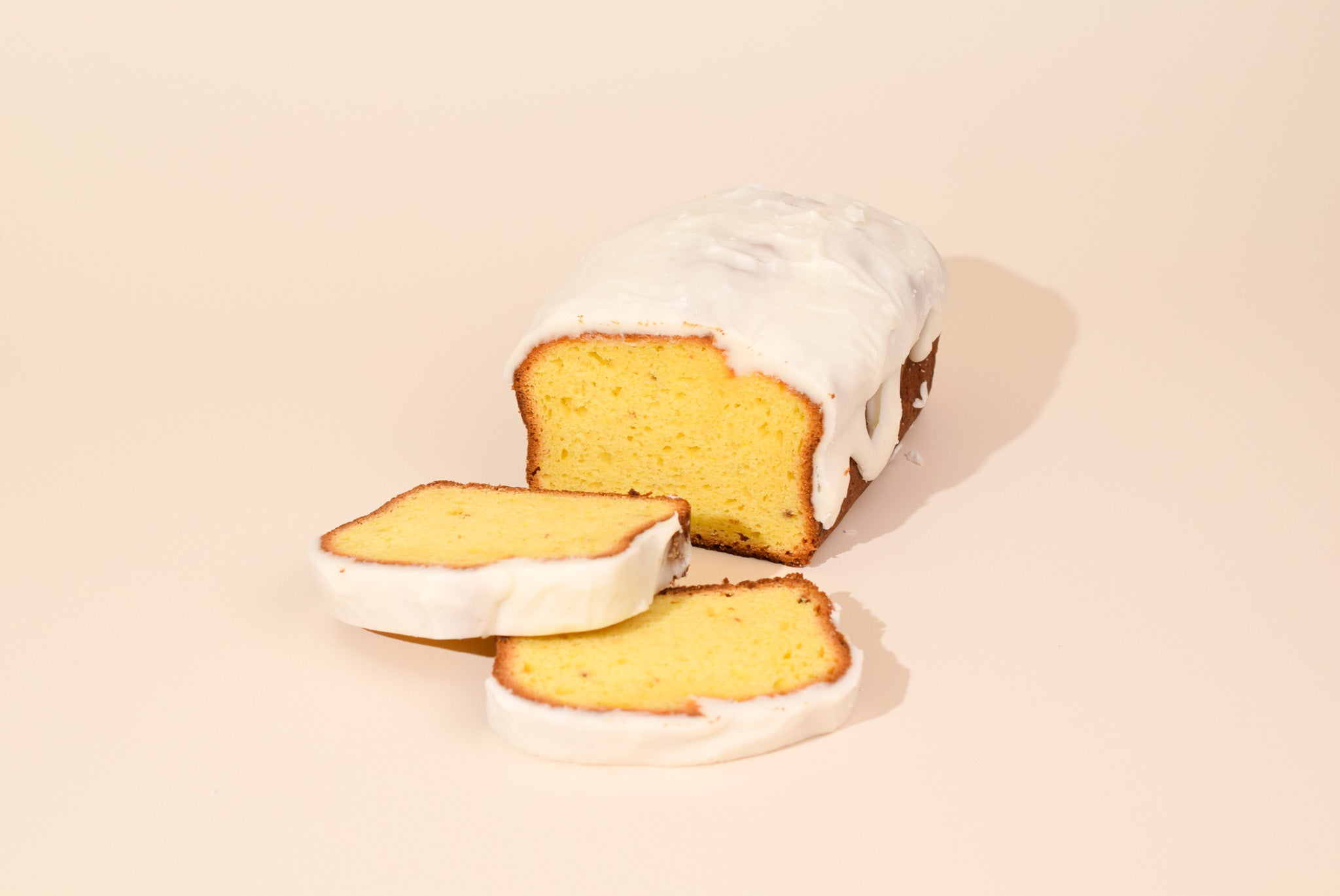 Keksi Iced Lemon Loaf with stacked slices on a cream background.