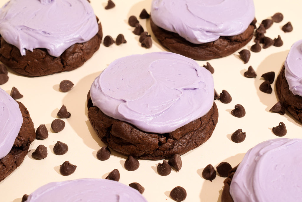 ghoulberry cookies topped with light purple frosting, arranged on a cream-colored surface with scattered chocolate chips.