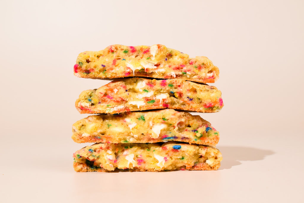 Four cut open birthday cake cookies stacked on a cream background.