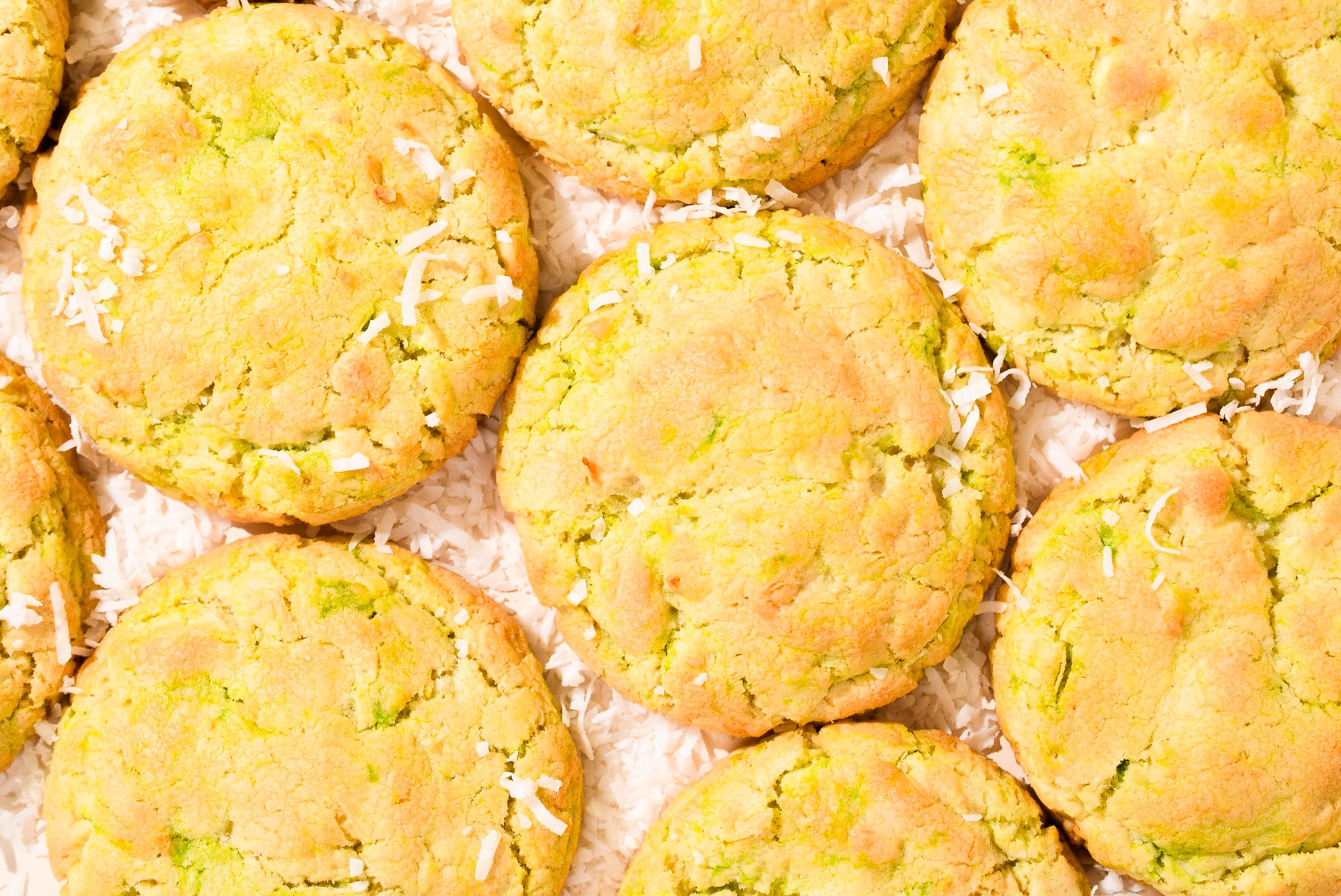 An overhead image of Key Lime Pie cookies with coconut shreds scattered on a cream background.