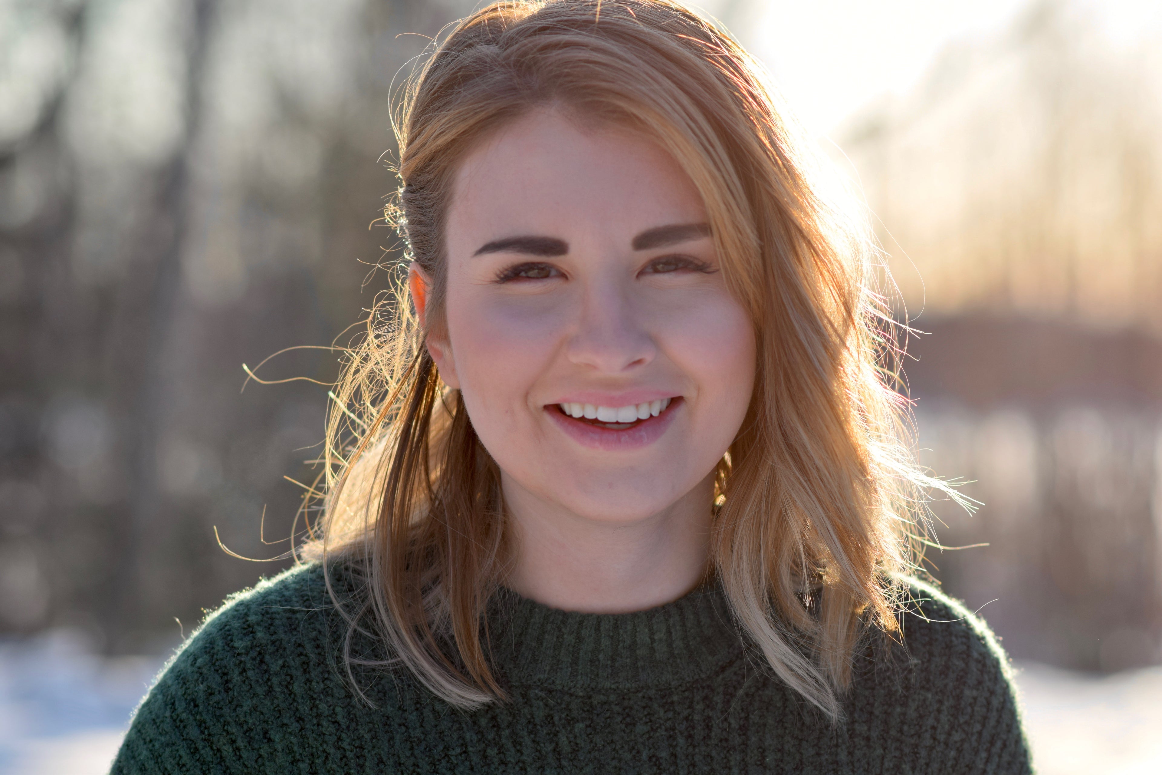 Woman with long blonde hair smiling outdoors in a blurred natural setting