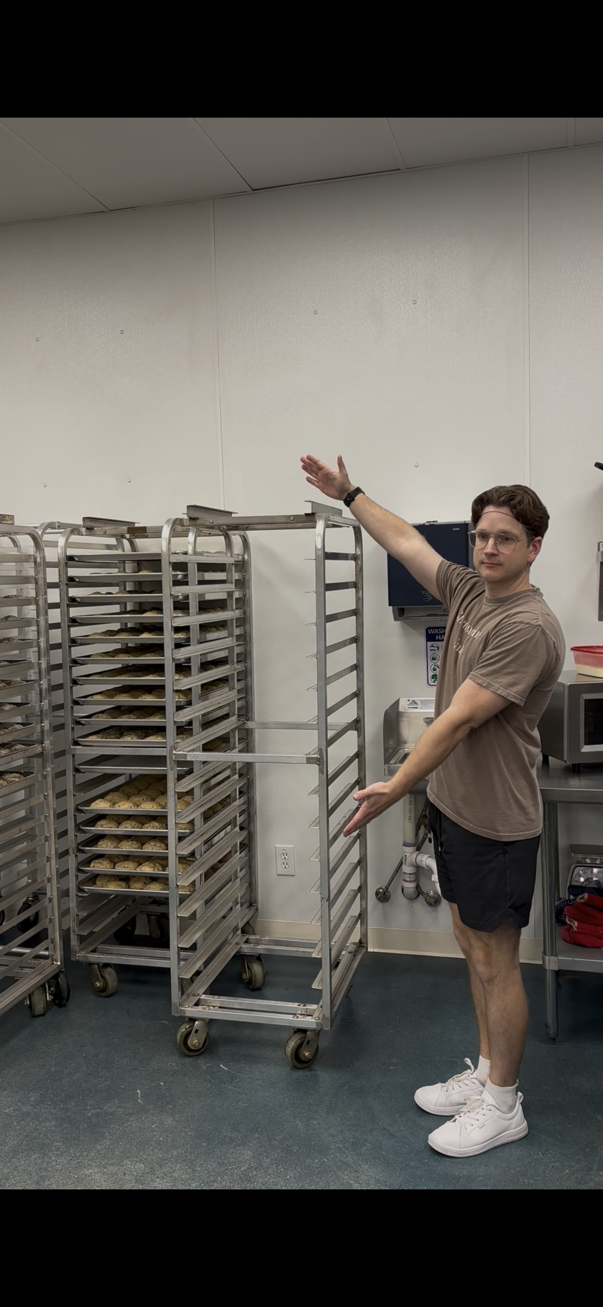 Person standing next to a rack of baking trays in a kitchen.