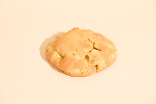 Caramel Macadamia cookie, whole with a craggy golden top, on a beige background
