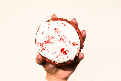 A hand holding a Keksi Blood Velvet cookie with white icing and red splatter