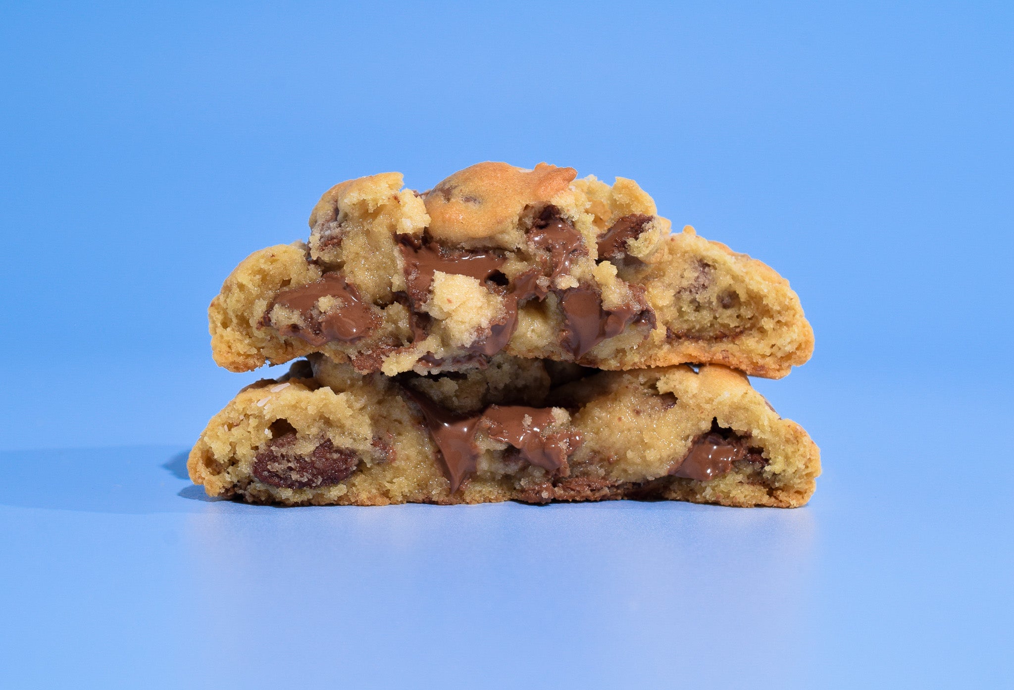 Two Texas Chocolate Chip cookies stacked on a blue background.