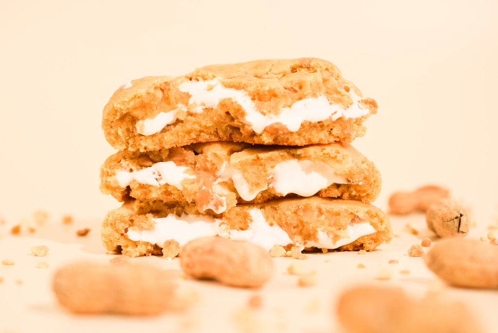 Peanut butter marshmallow cookies stacked with scattered peanuts on a cream background
